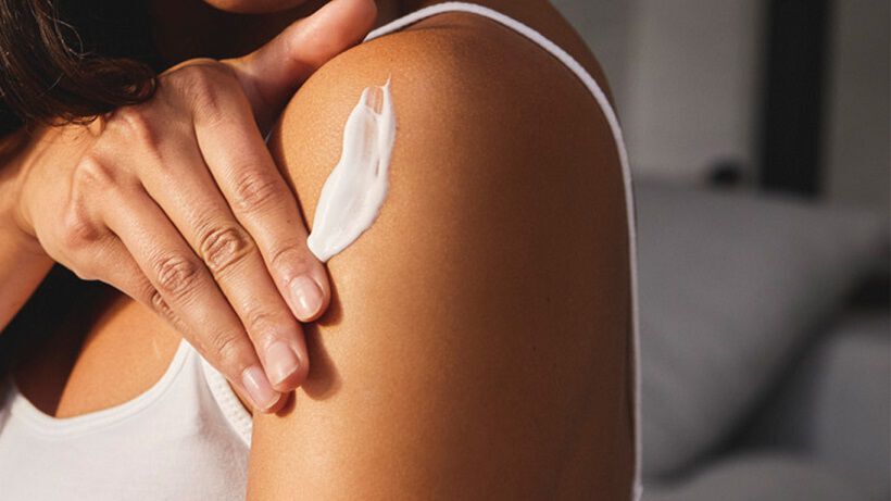 Vrouw smeert crème op haar bovenarm.